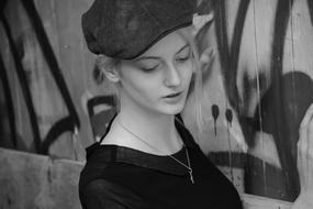 Black and white portrait of a beautiful, blonde girl in hat, near the wall with graffiti