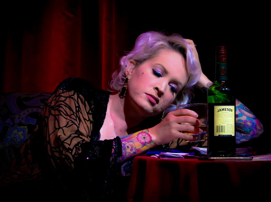 Woman with the colorful tattoos and white hair, sitting near the green bottle