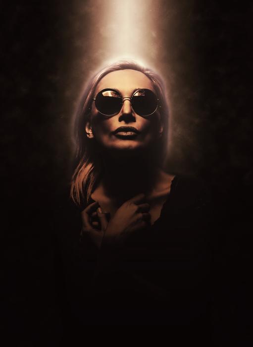 Woman in sunglasses with light on her on dark background