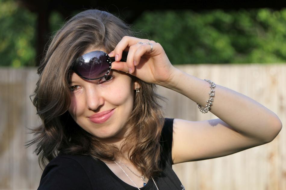 Portrait of Young Woman taking off sunglasses at background with the wooden fence and plants