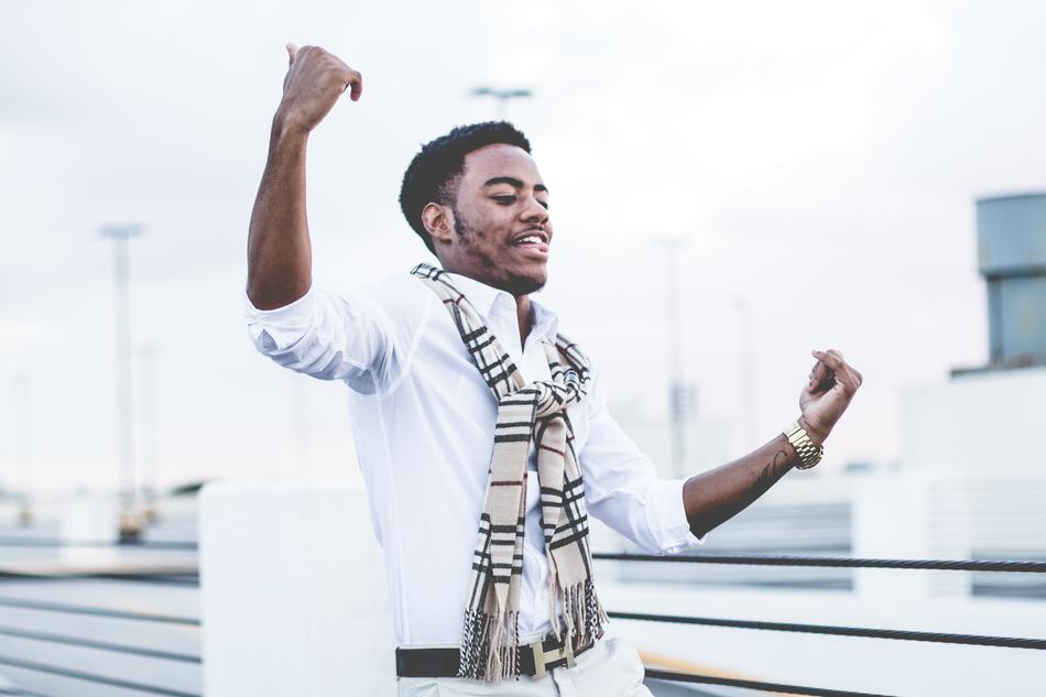 Afro American guy dancing in white shirt and pants by the fence