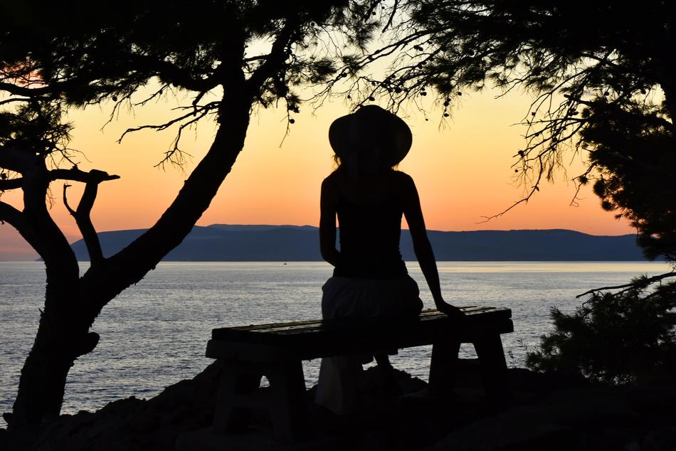 female silhouette on the bench on the beach at dusk