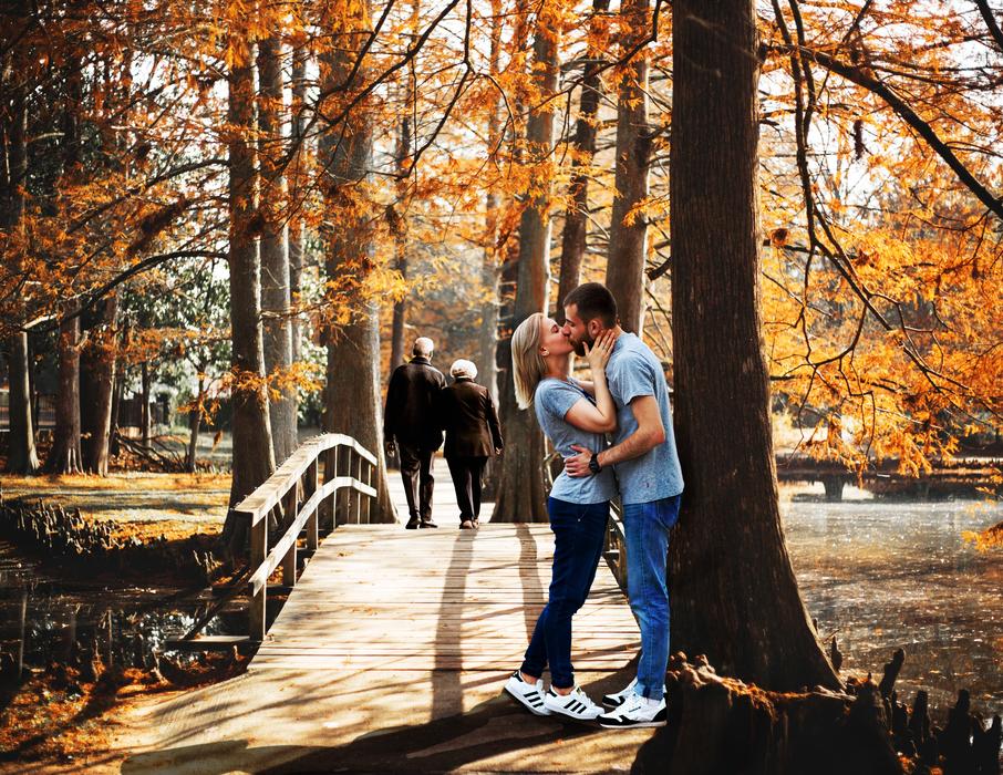young couple kissing in park beneath Tree at fall
