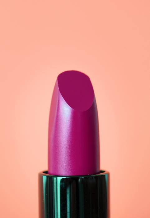 Close-up of the beautiful, shiny, purple lipstick, at gradient orange background