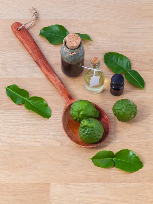 green limes on a wooden spoon and organic bottled oils on the table