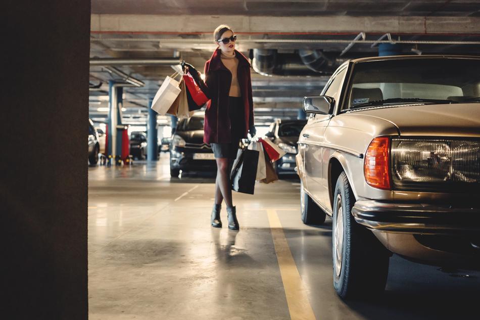 Woman, with the sunglasses and bags, on the high heels, walking on the carpark, among the cars