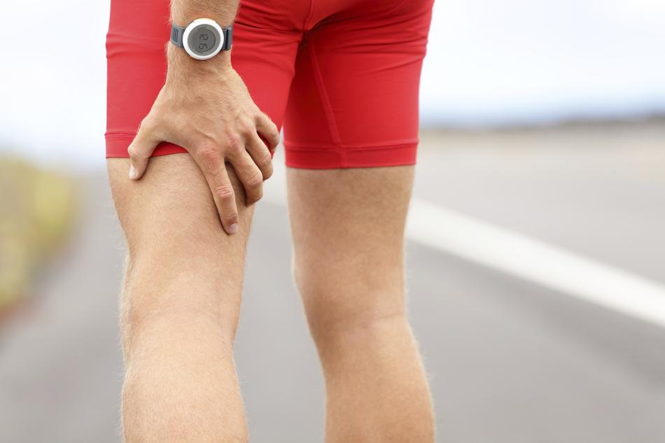 Close-up of the hand, with the wrist watch, on the leg of the runner, on the road