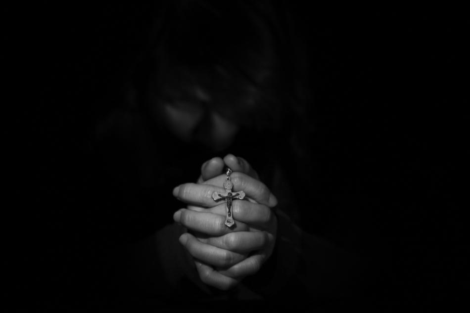 Black and white photo of the cross on closed hands in darkness