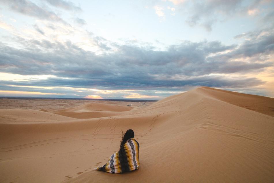 Woman sitting Alone on sand in desert at dusk