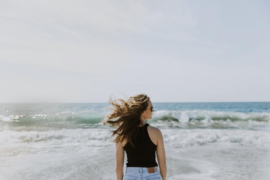 Back view of the girl with sunglasses and jeans, on the beautiful coast with waves