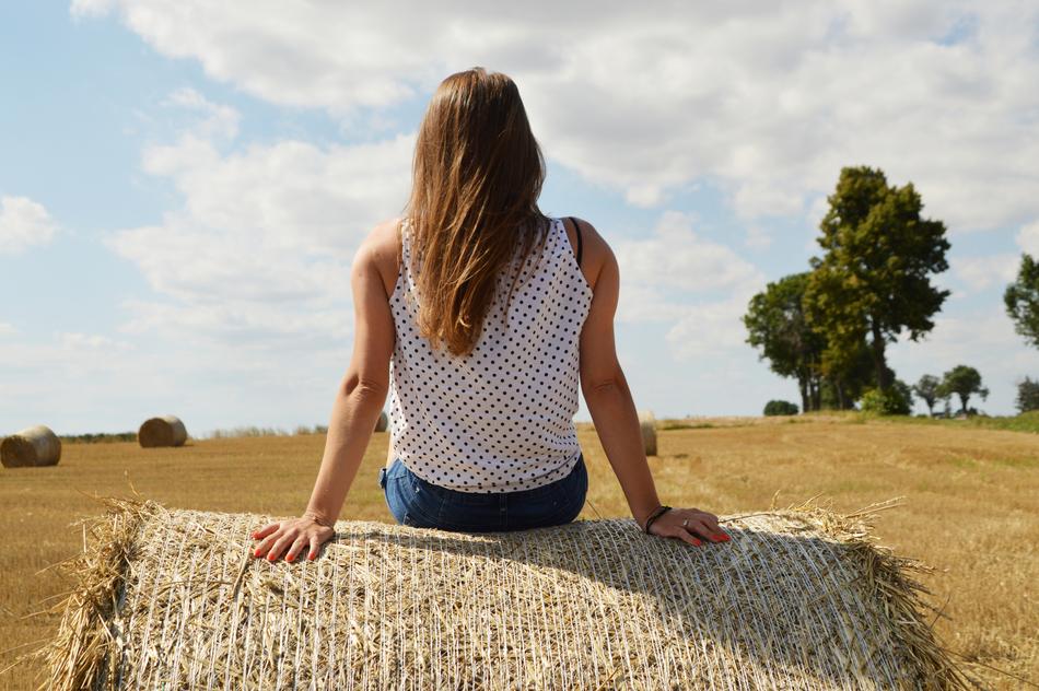 back view of girl sitting on hay ball on harvested field