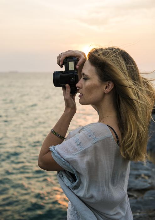 beautiful blonde with a camera on the coast at sunset