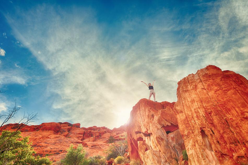 Woman, standing on the beautiful and colorful rock cliff, among the desert with green plants, in sunlight