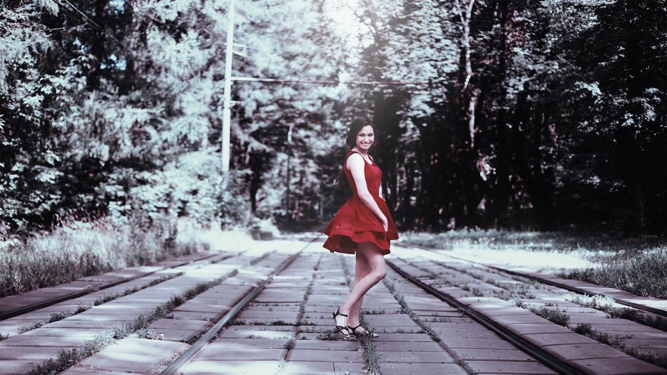 Vintage photo of the girl in red dress, posing on the beautiful tram road among the green trees
