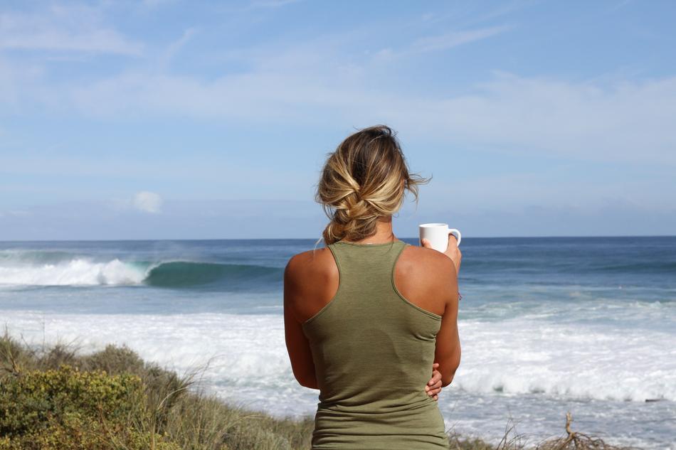Back view of a blonde girl, with white cup, on the beach of the ocean, with the waves
