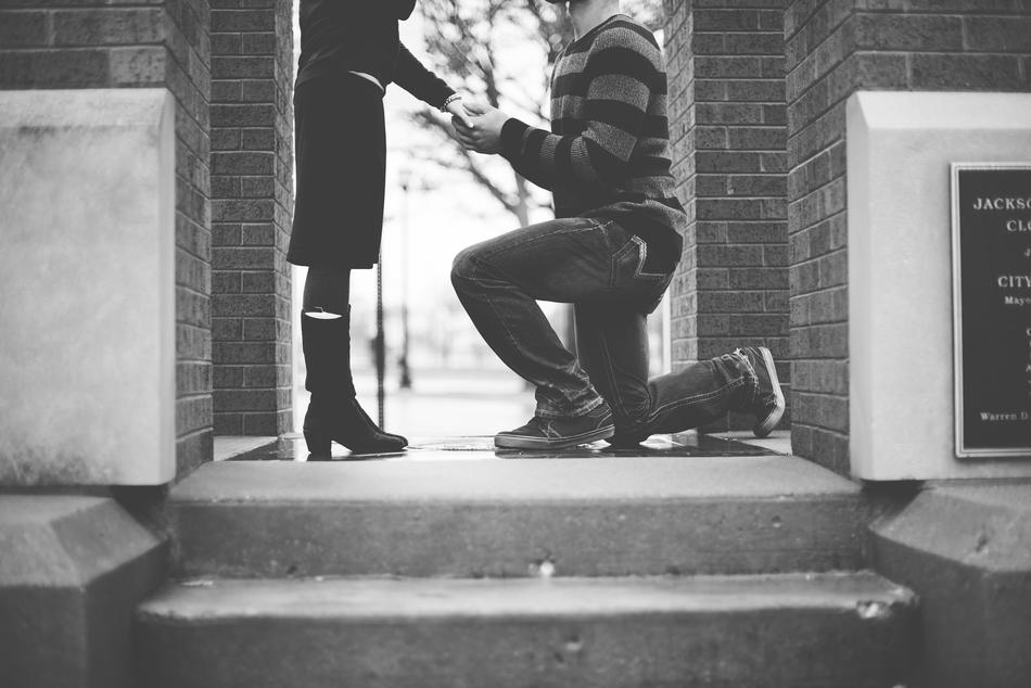 monochrome photo of unrecognizable man kneeling in front of woman on steps