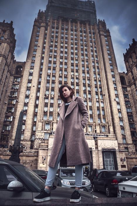 photo of a girl in a coat against a skyscraper