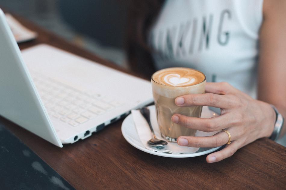 Woman, with the glass of coffee with beautiful heart drawing, near the white laptop