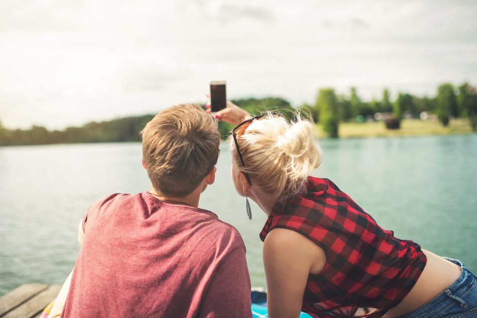 Back view of the blond couple, taking a selfie on the beautiful pier
