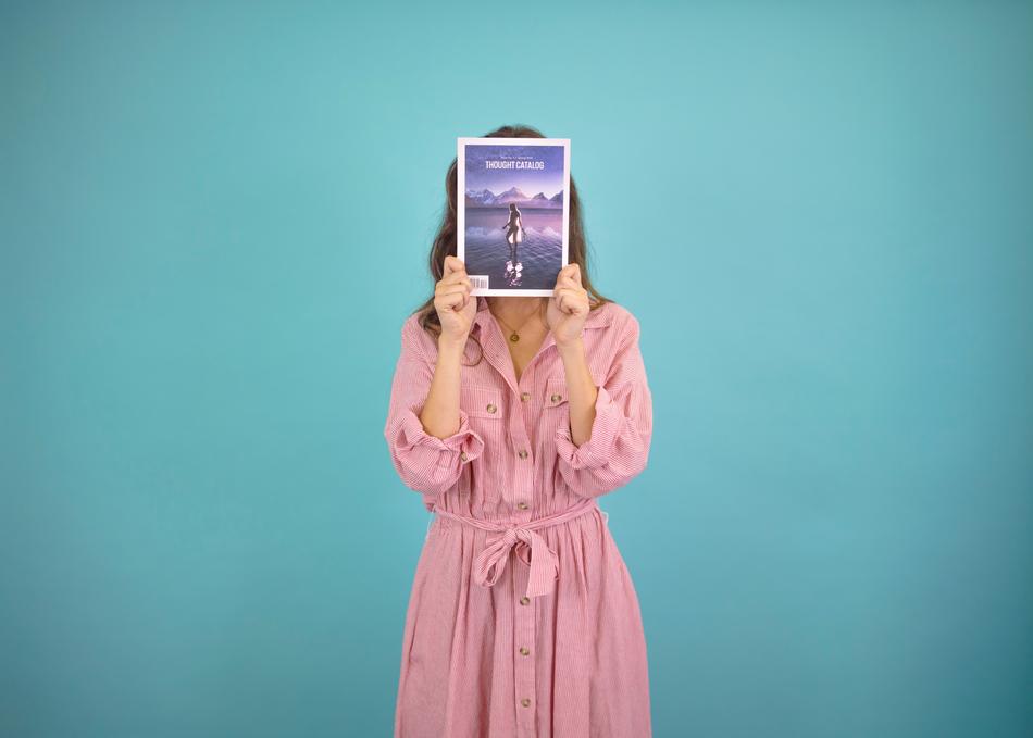 Woman in pink gown holding a book at face at blue background