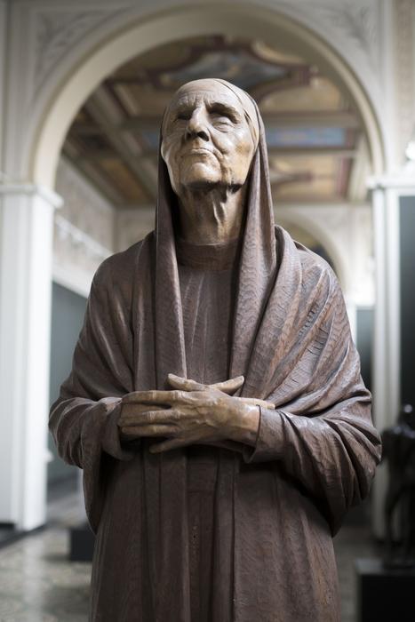 Sculpture of the religious woman, near the colorful arch of the building