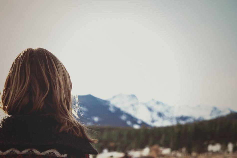 Back view of the woman, looking on the beautiful, snowy mountains, behind the green trees
