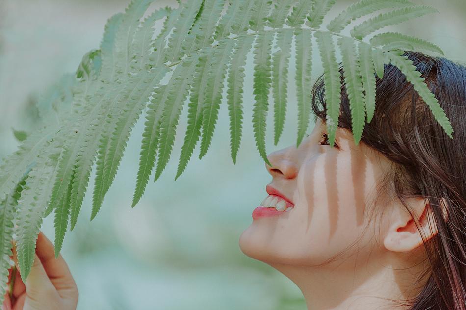 Profile portrait of the woman under green leaf in light