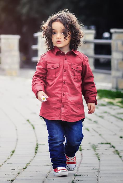 Cute child with curly hair, in red clothing and blue jeans, walking on the path