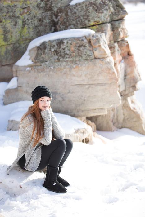 girl is sitting on a stone on the background of a snowy rock