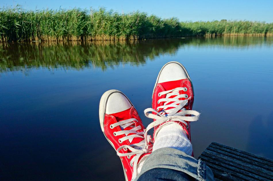 crossed legs in red sneakers on the background of the lake
