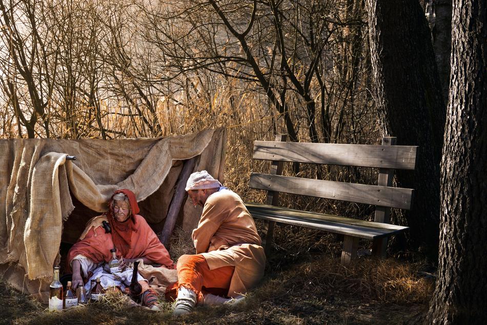 ragged man and woman with alcohol in bottles sitting on soil at tent