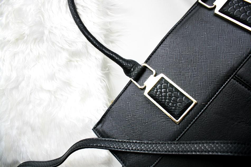Beautiful, black purse with the metal details, on the white, soft surface