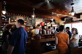 People, standing near the colorful bar in the restaurant, with the lights