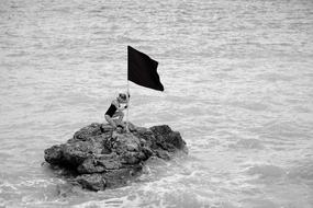 woman and flag on a stone in the ocean