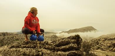 Woman with kettle bells in hands sits on mountain