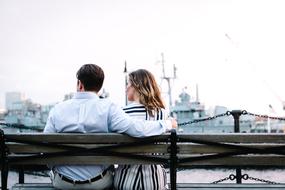 Back view of the couple, sitting on the bench, at buildings on background