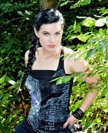 Black-haired woman in black and white clothing, posing near the green plants, in light