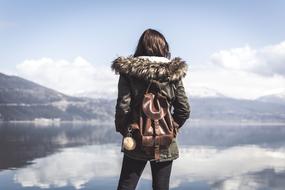 Woman with brown backpack standing near the beautiful lake