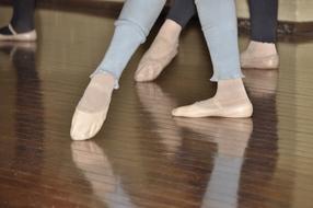 Close-up of the legs of the people, in the ballet shoes, with the reflections in the wooden floor