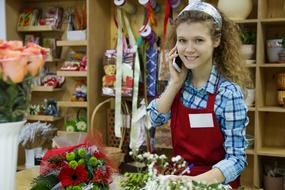 Portrait of the beautiful, smiling, blonde girl, with the curly hair, in the colorful flower shop, with the wooden shelves