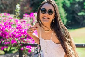 Portrait of the smiling woman, with the glasses and necklace, near the beautiful and colorful flowers