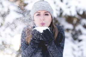 Woman in grey hat blowing on snow on her hands