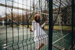 girl in white dress behind green fence