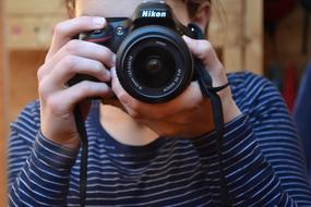 Woman in striped clothing, taking a photo with "Nikon" camera
