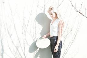 Blonde girl, posing near the wall with the shadows of the branches, in light