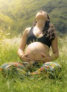 Pregnant woman in black bra, sitting on the colorful and beautiful field