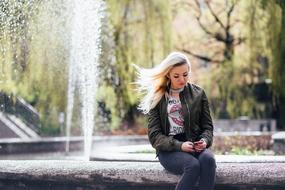 girl with mobile phone near the fountain in the park