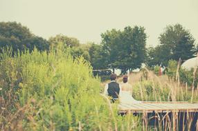 the bride and groom sit on the boardwalk near the river