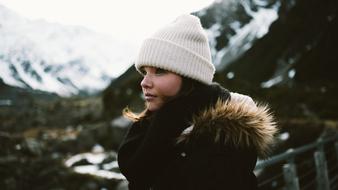 Profile portrait of the beautiful girl in hat and jacket, near the snowy mountains