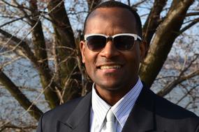 Portrait of the smiling man with glasses, in suit and shirt with tie, near the tree